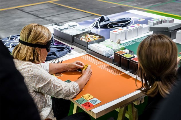 Am Spieltisch sitzen Teilnehmende mit verbundenen Augen und probieren die Spiele aus